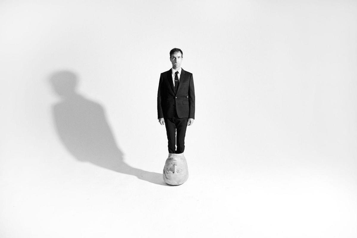 Andrew Bird standing in stone head white studio