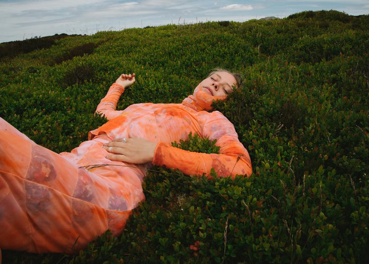 Anna B Savage in orange suit lying in grass