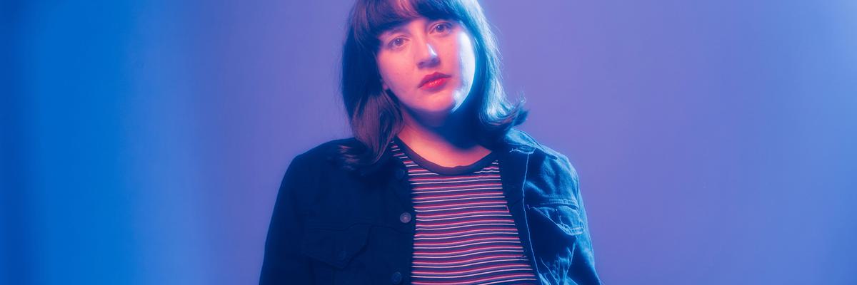 Caitlin Rose with hands in pockets in blue and purple lighting