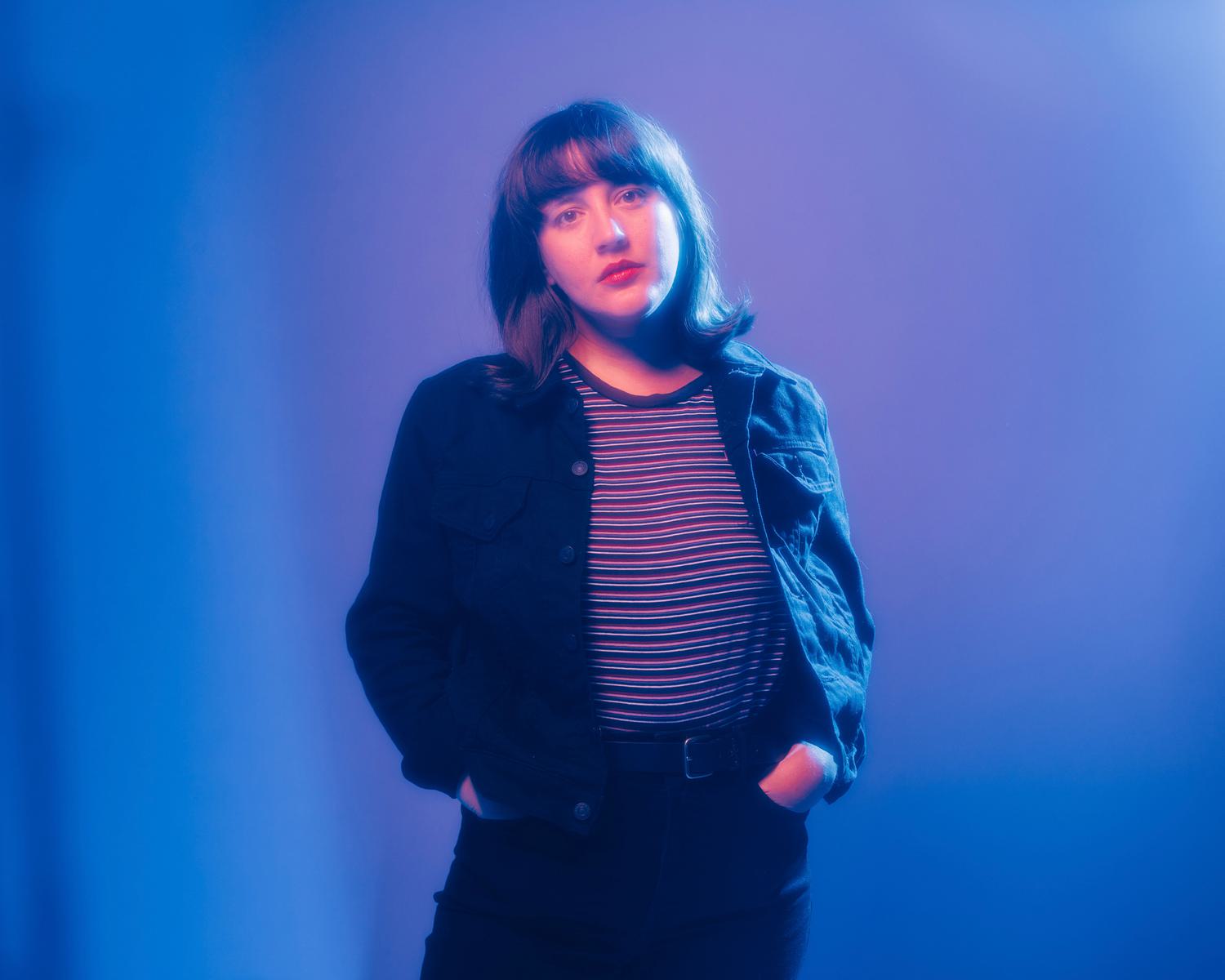 Caitlin Rose with hands in pockets in blue and purple lighting