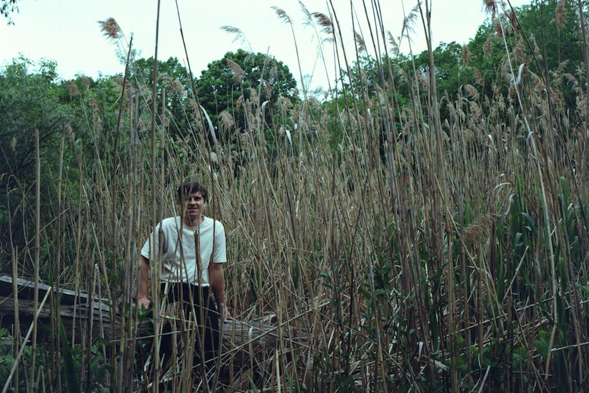 Leland Whitty sitting on fallen tree in white t shirt