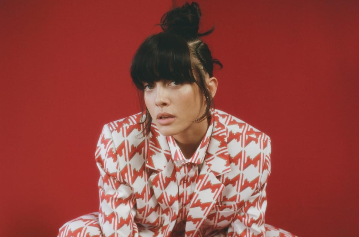 Noga Erez crouching in red patterned suit