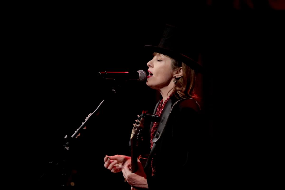 Suzanne Vega in a black hat singing into a mic