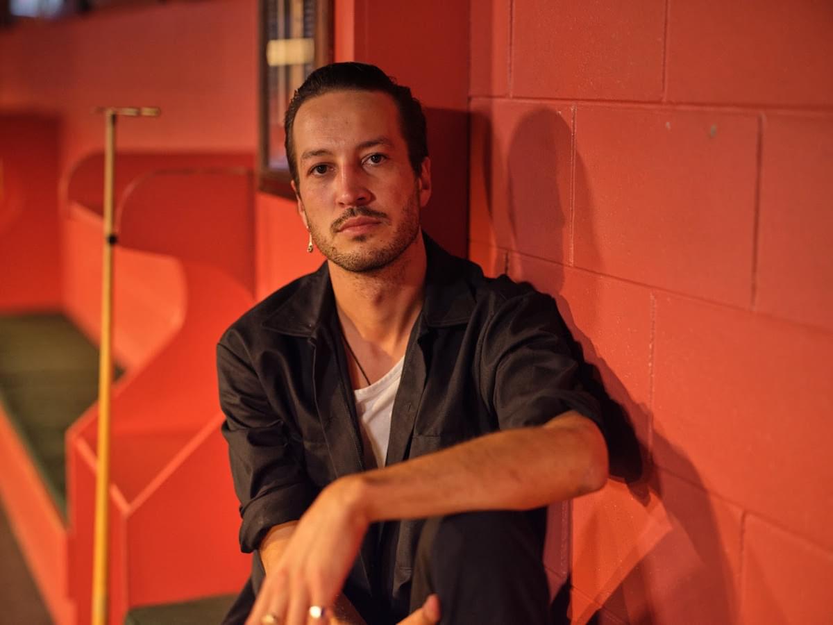 Marlon Williams sat against a red wall for "Don't Go Back" single