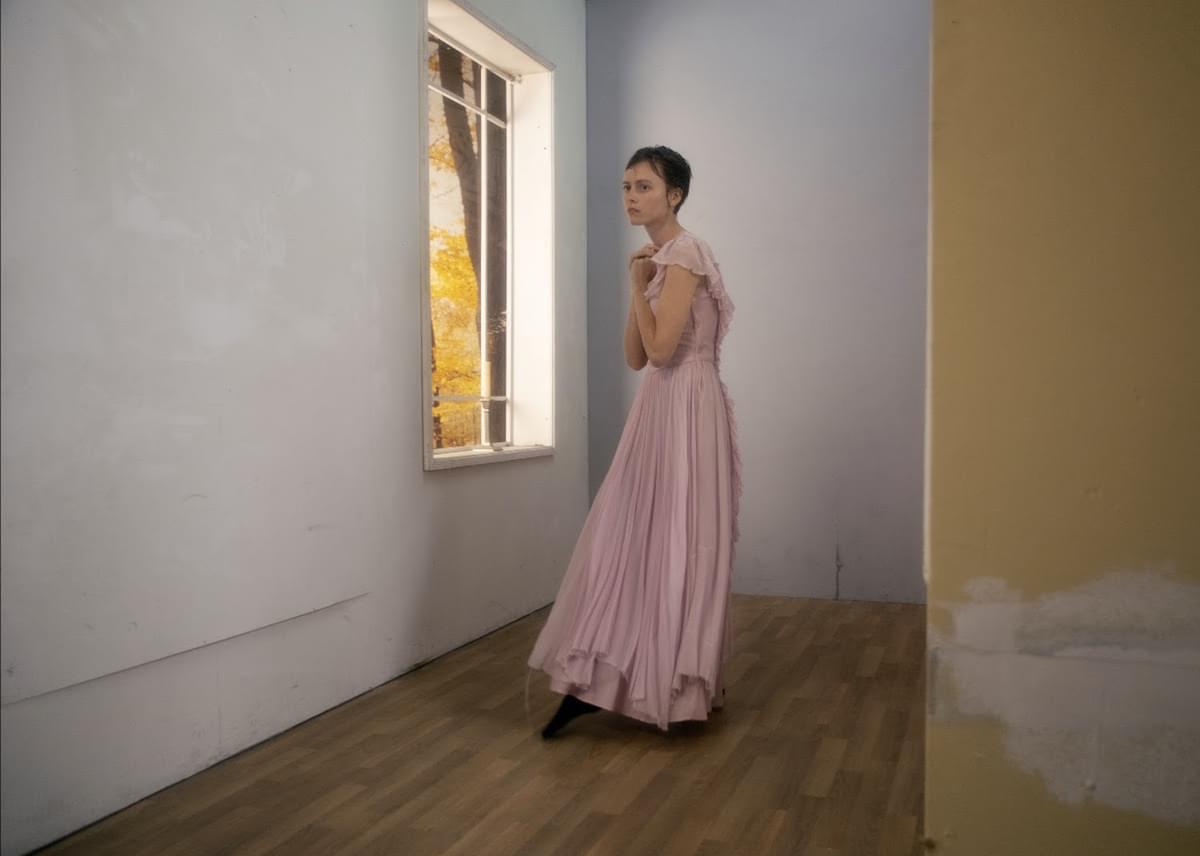 Skullcrusher in an empty room wearing long pink dress for "It's Like A Secret" single